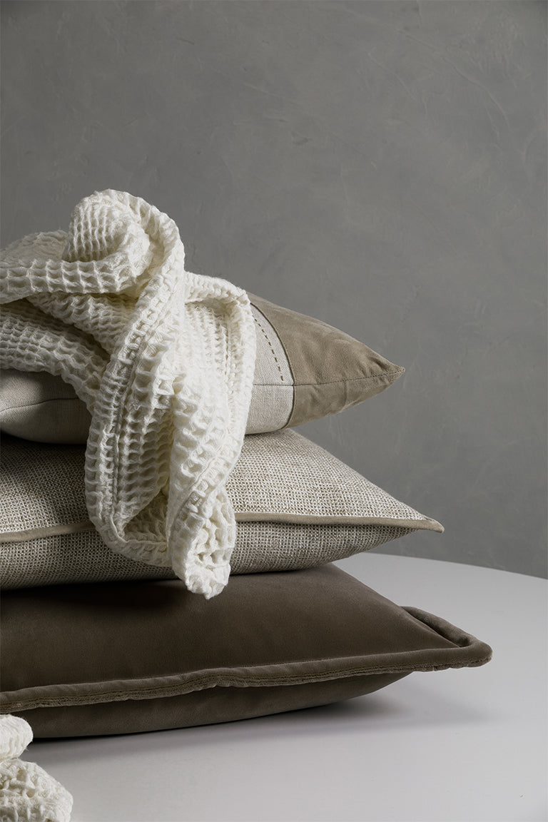 Stack of cushions with a textured blanket on a neutral background