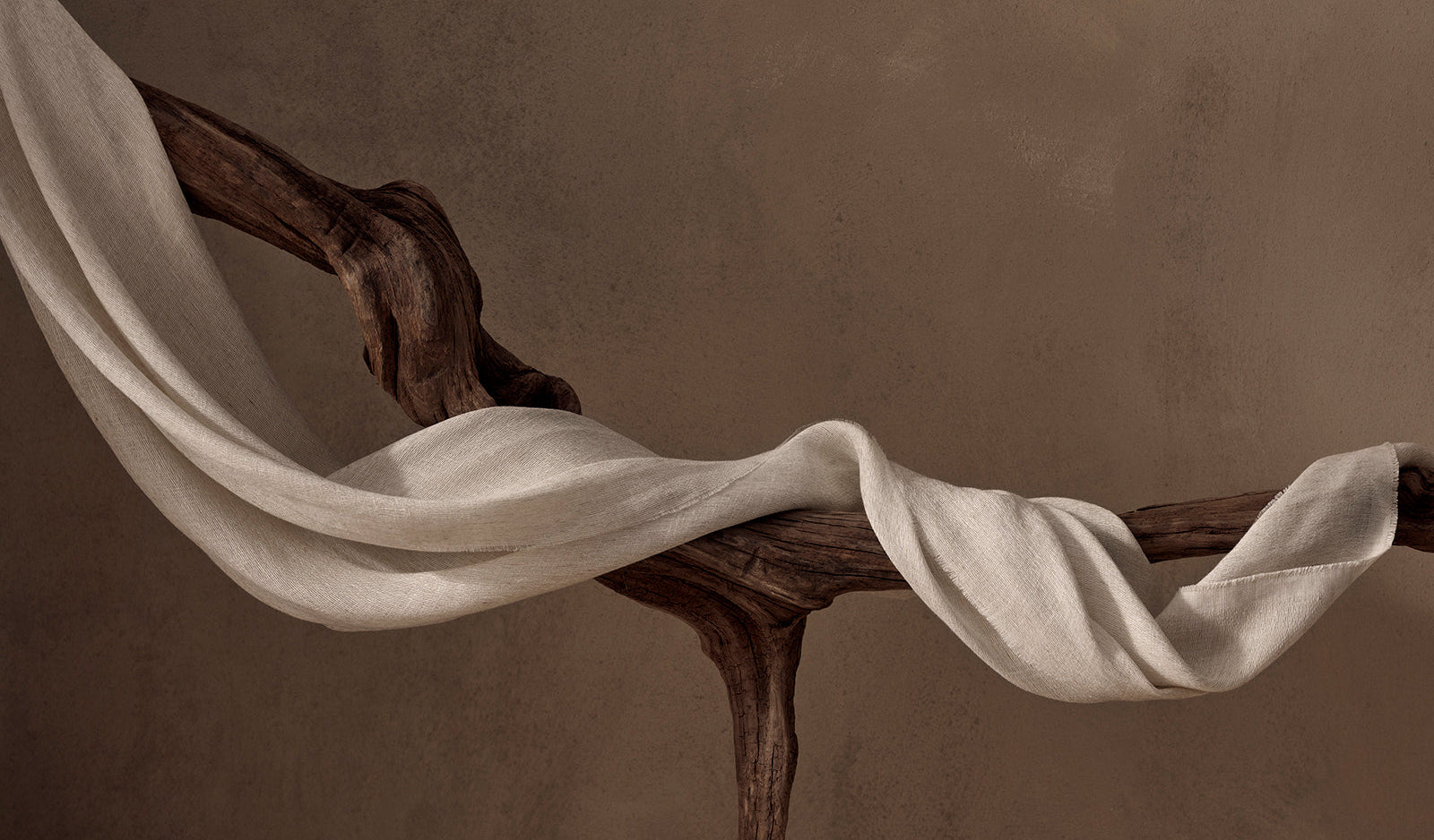 White fabric draped over a wooden branch against a brown background